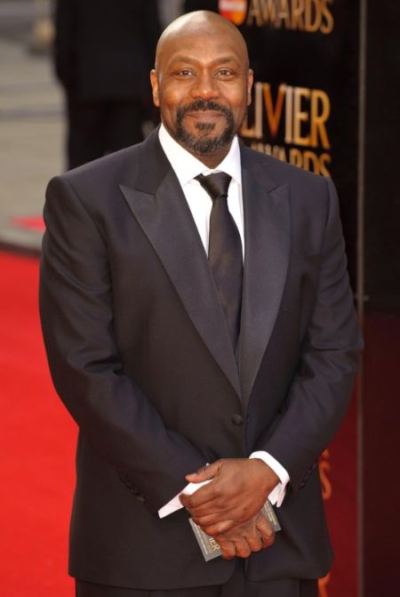 Lenny Henry in a black suit and black tie poses for a picture.